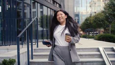 Business-Chinese-woman-walking-down-the-stairs-with-phone-and-cup-of-coffee
