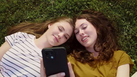 Top-view-of-best-friends-lying-on-grass-with-mobile-phones