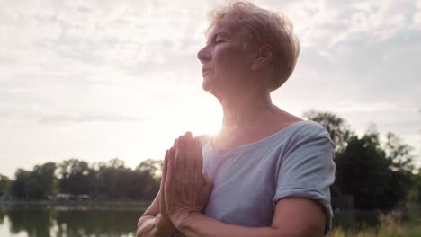 Calm-senior-woman-meditating-in-the-park-by-the-lake