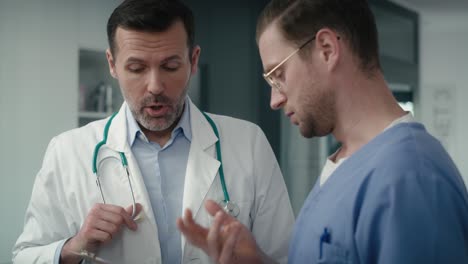 Two-serious-caucasian-male-doctors-discussing-over-documents-in-medical-clinic