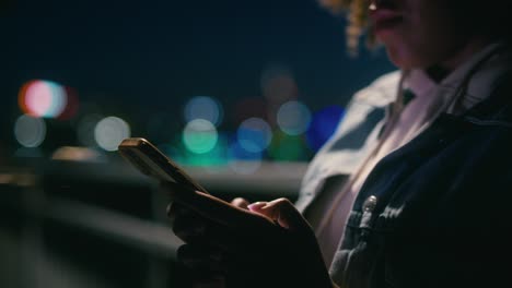 Detail-of-black-woman-standing-on-the-bridge-at-night-and-browsing-her-mobile-phone