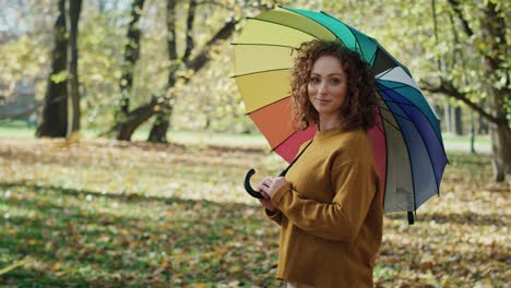 Portrait-of-caucasian-woman-with-colorful-umbrella-standing-in-the-park.
