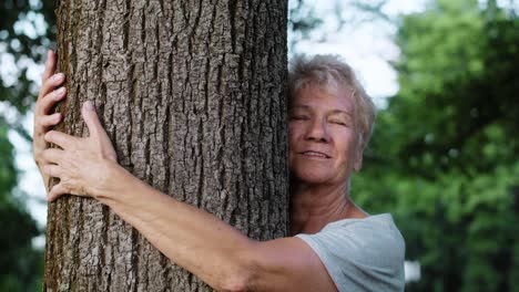 Cheerful-senior-woman-embracing-tree-in-the-park.