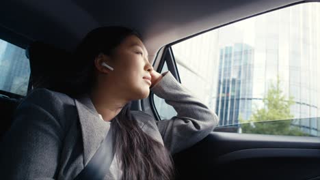 Mujer-China-De-Negocios-Conduciendo-En-Un-Taxi-Y-Usando-Auriculares