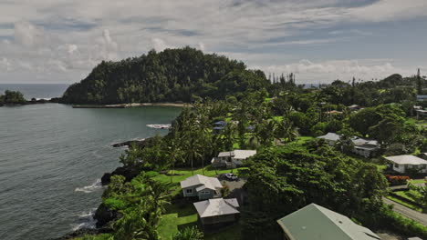 Hana-Maui-Hawaii-Aerial-v9-drone-fly-along-the-rugged-coastline-capturing-seaside-residential,-coastal-town,-black-sand-beach-and-community-park-in-summer---Shot-with-Mavic-3-Cine---December-2022