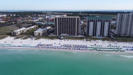 Zoom-in-Aerial-shot-of-waterfront-resort-with-colorful-umbrella-and-beach-chair-on-the-sandy-beach-shore-of-gulf-of-mexico-in-Fort-Walton-beach-Okaloosa-island-in-Destin-Florida