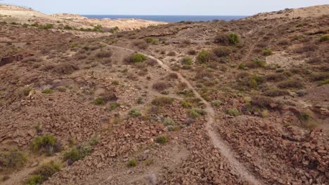 Drone-Retreats-Over-Sunlit,-Arid-Mountains-by-Tenerife’s-Sea