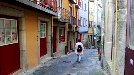 Caucasian-woman-with-backpack-walking-down-street-with-colourful-houses-in-Porto