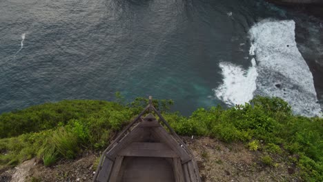 Adult-person-at-Paluang-cliff-of-Nusa-Penida-sitting-on-ship-bow-viewpoint-platform-and-photo-spot-with-view-to-kelingking-seascape