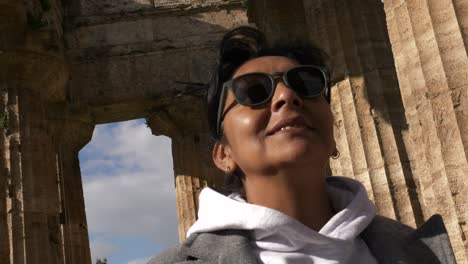 Woman-with-sunglasses-smiling-at-life-visiting-a-Greek-temple-during-a-sunny-day