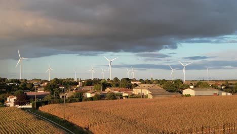 Turbinas-Eólicas-Girando-Contra-Un-Cielo-Azul-Con-Una-Nube-De-Tormenta-Gris-Oscuro-Arriba-Con-Lluvia-A-La-Vista-Con-Un-Pueblo-Francés-Debajo