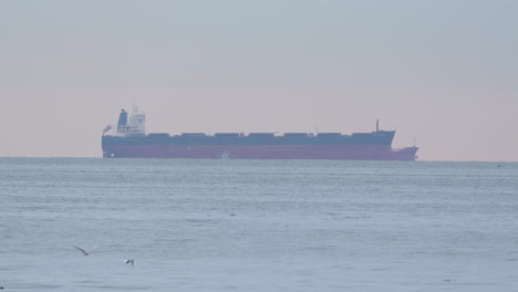A-huge-cargo-ship-vessel-is-anchored-at-sea-in-calm-waters-and-with-seagulls-flying-by