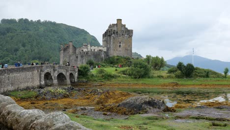 Eilean-Donan-Castle-with-a-stone-bridge-full-of-tourists-visiting-the-landmark-in-cloudy-Scottish-weather