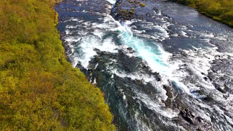 Siga-El-Flujo-De-Agua-Por-Drones-De-La-Hermosa-Cascada-De-Bruarfoss-Con-Agua-Turquesa-En-Islandia