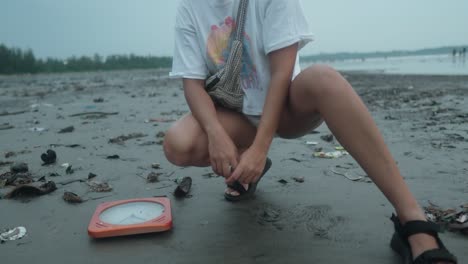 Girl-Next-to-a-wall-Clock-that-Sank-on-the-Black-Sand-Beach-Full-of-Trash