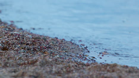 A-close-up-view-of-calm-ocean-waves-hitting-small-pebbles-on-the-beach