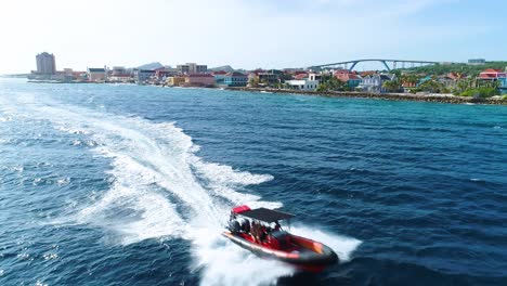 Super-rib-inflatable-boat-drives-quickly-along-coast-of-Willemstad-Curacao,-aerial-tracking-follow