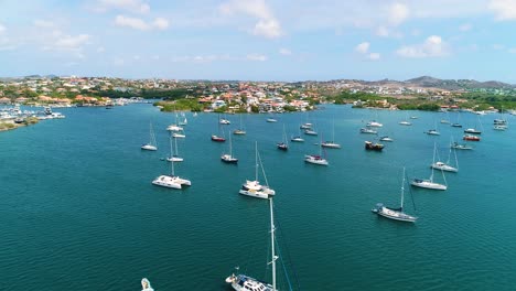 Aerial-trucking-pan-across-catamaran-sailboats-anchored-in-Caribbean-bay-of-Spanish-Waters,-Curacao