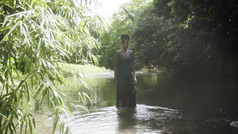 Woman-wearing-a-green-dress-stands-deep-in-thought-in-a-river