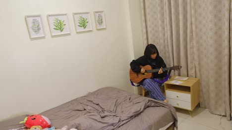 Bonita-Chica-Asiática-Practicando-Guitarra-Acústica-En-La-Esquina-De-La-Habitación.