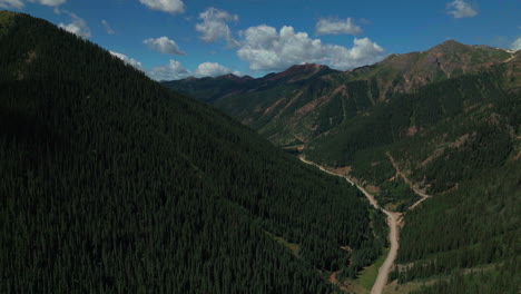 Aerial-cinematic-drone-summer-high-altitude-dirt-road-Silverton-Mountain-Ski-Resort-southern-Colorado-blue-sky-late-morning-stunning-lush-green-blue-sky-partly-cloudy-Rocky-Mountains-forward-motion