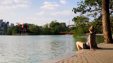 Cityscape-of-Hanoi-in-the-background-a-young-woman-relaxes-at-Hoan-Kiem-Lake