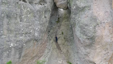 Drone-view-of-a-Man-climbing-a-ladder-in-Karadzhov-kamak-in-Rhodope-mountain,-Bulgaria