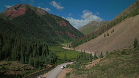 Aerial-drone-cinematic-Ice-Lake-Basin-trailhead-driving-camper-van-county-road-river-summer-early-morning-Silverton-Telluride-Colorado-Rocky-Mountains-Aspen-forest-14er-peaks-forward-follow-motion