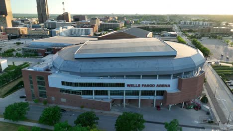 Aerial-view-descending-towards-the-Wells-Fargo-Arena-with-the-Des-Moines-cityscape-in-the-background,-illuminated-by-early-morning-light