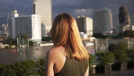 A-young-woman-with-auburn-hair-gazes-out-at-the-impressive-Bangkok-skyline-on-a-clear-day