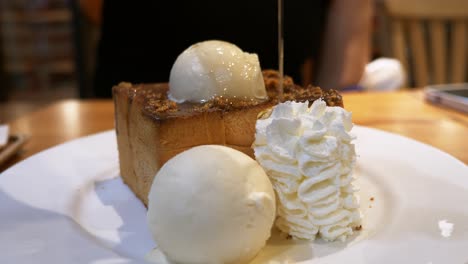 Drizzling-some-honey-over-a-decadent-bread-toast,-topped-with-vanilla-ice-cream,-nuts,-caramel-sauce,-and-whipped-cream-on-the-side
