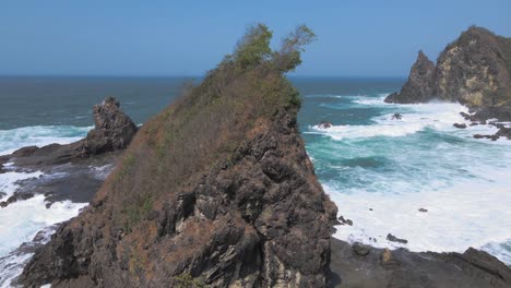 On-the-beach-of-Watu-Lumbung-in-Indonesia,-waves-crash-white-foaming-on-the-coral-rocks