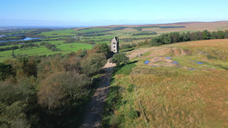 Flying-fast-over-track-towards-lone-stone-tower-building-on-hillside-with-reveal-of-countryside-beyond