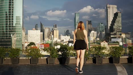 Eine-Junge-Frau-Geht-Auf-Einem-Dach-Eines-Hotels-Langsam-Auf-Die-Atemberaubende-Skyline-Von-Bangkok,-Thailand,-Zu