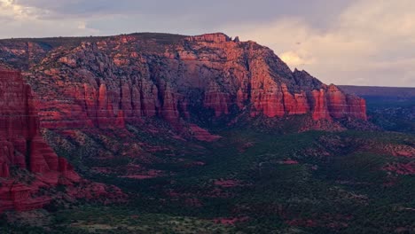 Purple-red-shadows-and-light-spread-across-sheer-sandstone-mountains-of-Sedona-Arizona-at-dusk,-drone