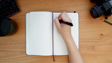 Overhead-shot-of-handwriting-in-a-black-notebook-on-a-wooden-desktop