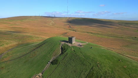 Hilltop-with-stone-structure-and-tall-radio-transmitter-on-hilltop-behind,-autumnal-colours