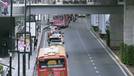 Daily-traffic-situation-in-Bangkok,-left-lane-is-slow-as-busses-stop-at-Bus-Stop-stations-while-commuters-walk-on-the-sidewalk-and-crossing-the-bridge