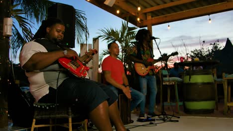 Reggae-artists-and-band-strum-guitar-and-hit-drums-at-sunset-performing-and-singing
