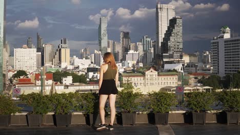 A-scenic-panorama-view-of-a-young-beautiful-woman-looking-out-over-the-city-skyline-of-Bangkok,-Thailand