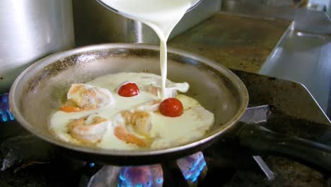 El-Chef-Rocía-Crema-Espesa-En-Una-Sartén-Sobre-Una-Estufa-De-Gas-Con-Camarones,-Tomates-Y-Salsa-Blanca-Lechosa.