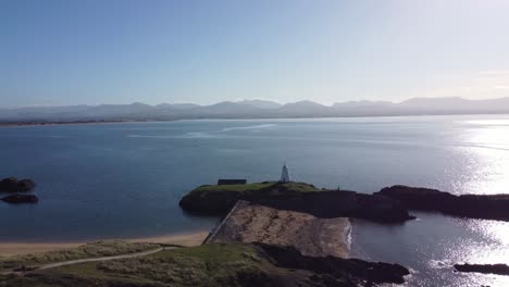 Aerial-view-across-idyllic-Ynys-Llanddwyn-island-with-hazy-Snowdonia-mountain-range-across-shimmering-Irish-sea-towards-lighthouse