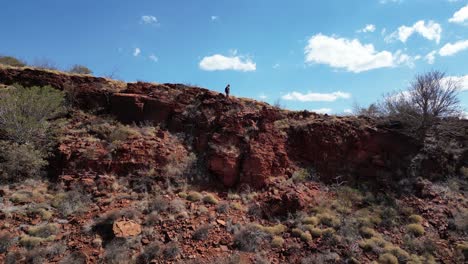 Aerial-view-of-hiker-on-edge-of-red-mountains-in-Karijini-National-Park-during-sunny-day-in-Australia