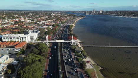 Aerial-view-of-busy-coastal-road-with-traffic-at-Swan-River-in-Perth-City-during-sunset-time,-Australia---tilt-up