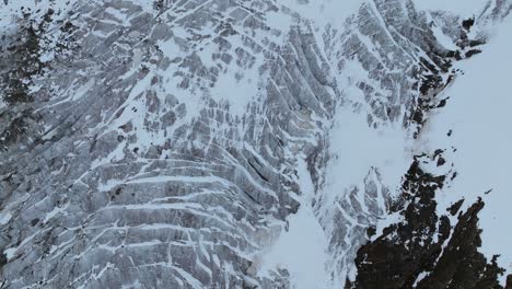A-breathtaking-top-down-view-captures-the-intricate-patterns-of-a-glacier-juxtaposed-against-rugged-mountain-terrain