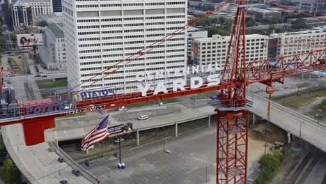 Eine-Umlaufende-Luftaufnahme-Zeigt-Einen-Baustellenkran-In-Der-Stadt-Atlanta-Mit-Wehender-Amerikanischer-Flagge