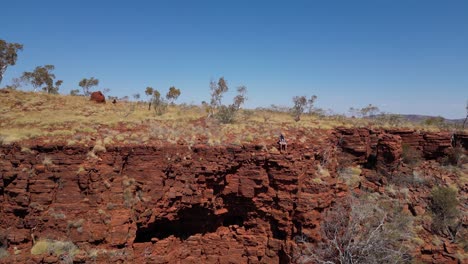Epic-drone-shot-showing-man-sitting-on-edge-of-cliff-in-Australian-desert-mountains-against-blue-sky