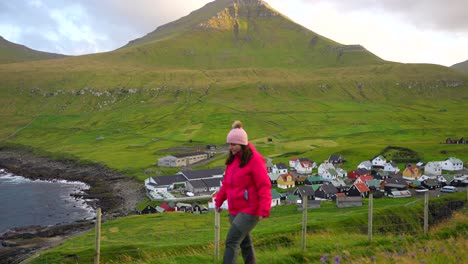 Mujer-Caminando-Cerca-Del-Hermoso-Pueblo-De-Gjogv-Y-Las-Montañas-En-Eysturoy,-Islas-Feroe