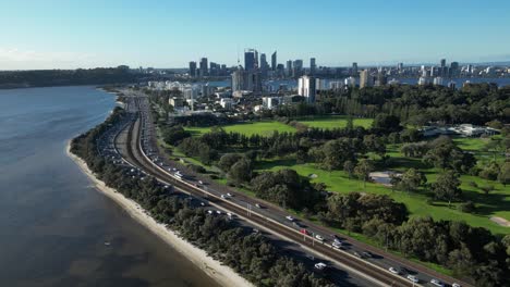 Drone-shot-of-high-frequented-coastal-intersection-beside-golf-course-and-Perth-skyline-in-background---beautiful-sunny-day-in-Australia