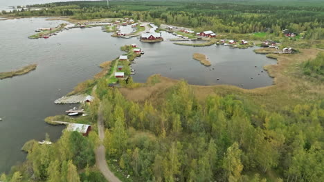 Fliegen-Sie-über-Die-Herbstliche-Seenlandschaft-Mit-Roten-Hütten-An-Einem-Bewölkten-Tag-In-Finnland